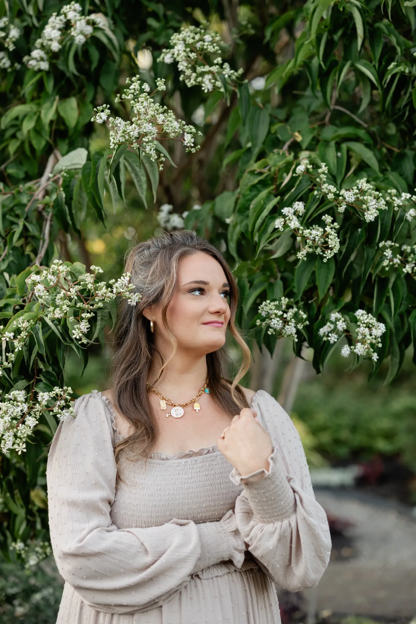 Woman standing under a tree adorned with white blossoms, looking peacefully upward.