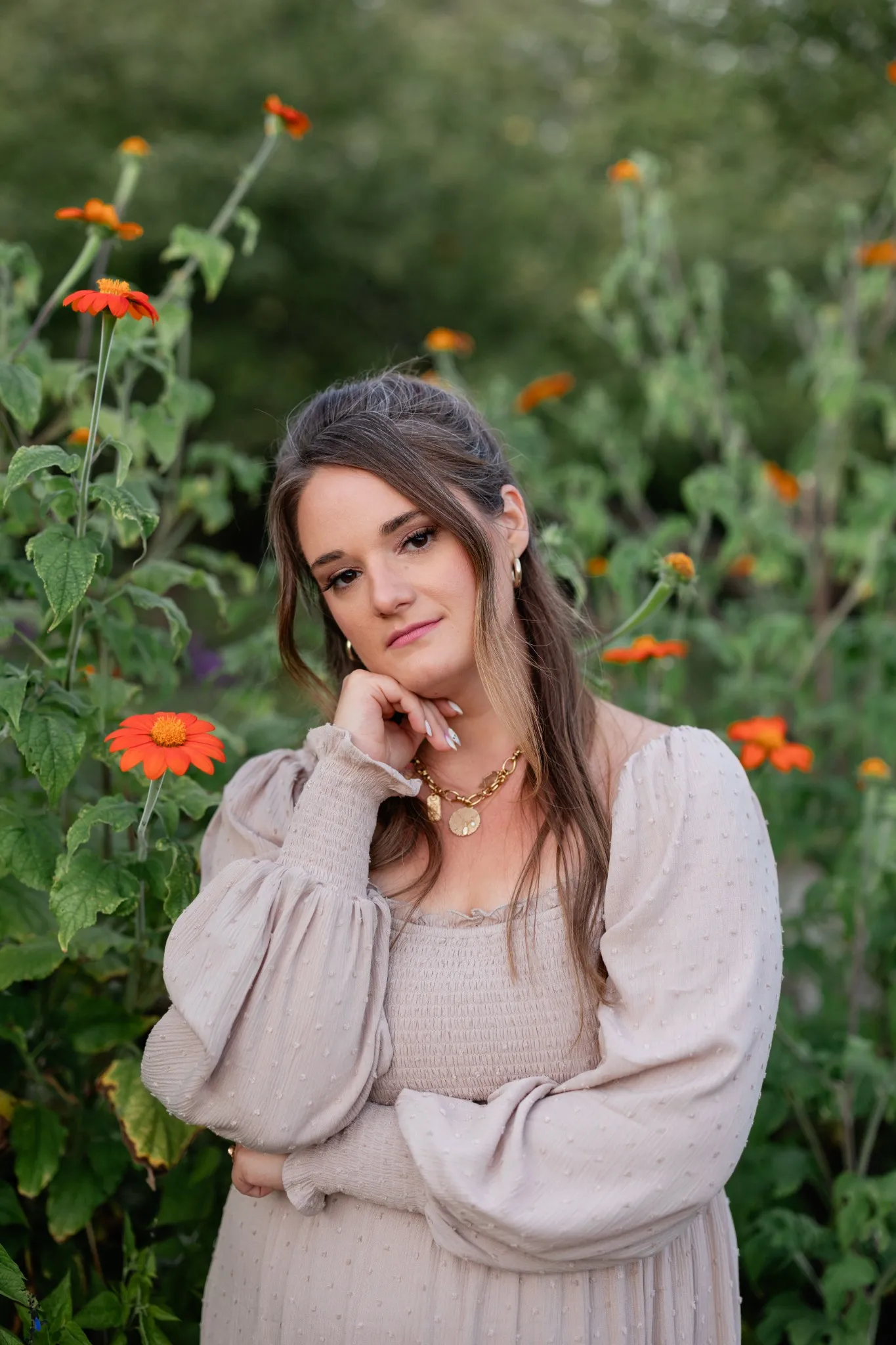 Woman in a garden surrounded by tall orange flowers, hand resting on her chin.