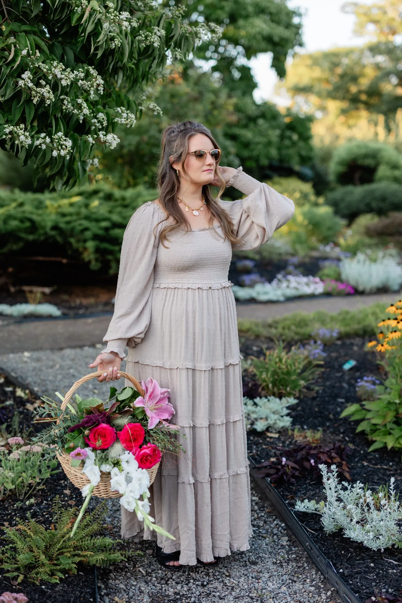 Woman in a flowing dress holding a basket of flowers, walking through a garden surrounded by white blossoms.